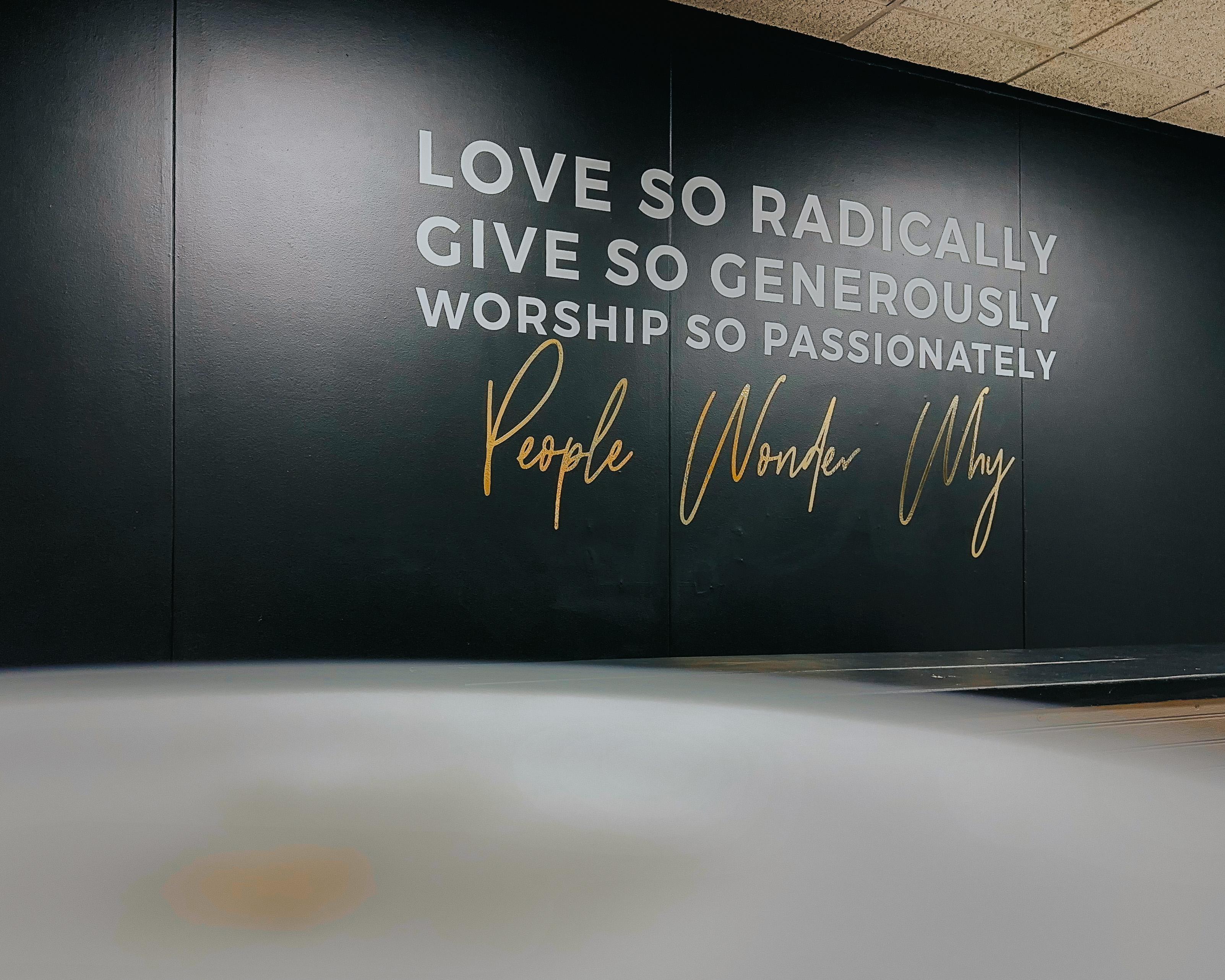 Church wall quote - Love So Radically, Give So Generously, Worship So Passionately - gold script on dark wall