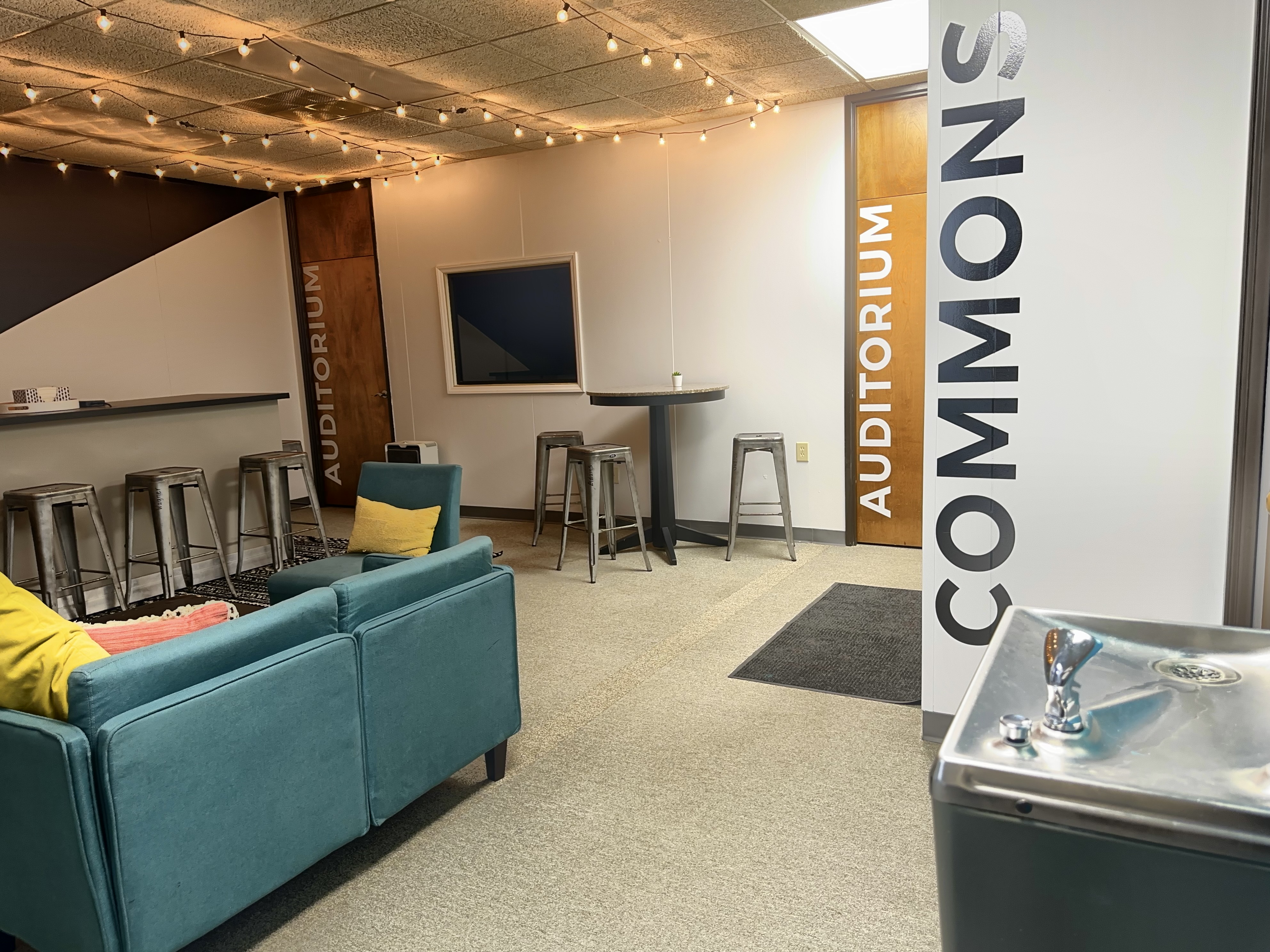 Church commons area with string lights, couches, and auditorium signage